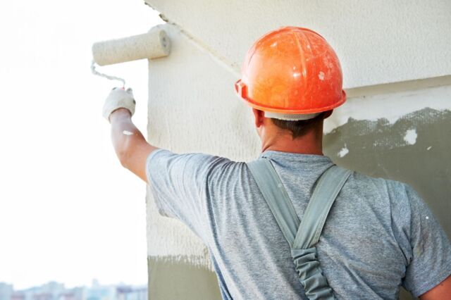 Een man die de buitenkant van een muur verft 